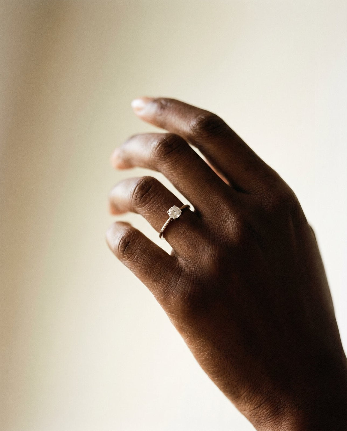Hand raised against a soft background wearing a lab-grown diamond solitaire ring