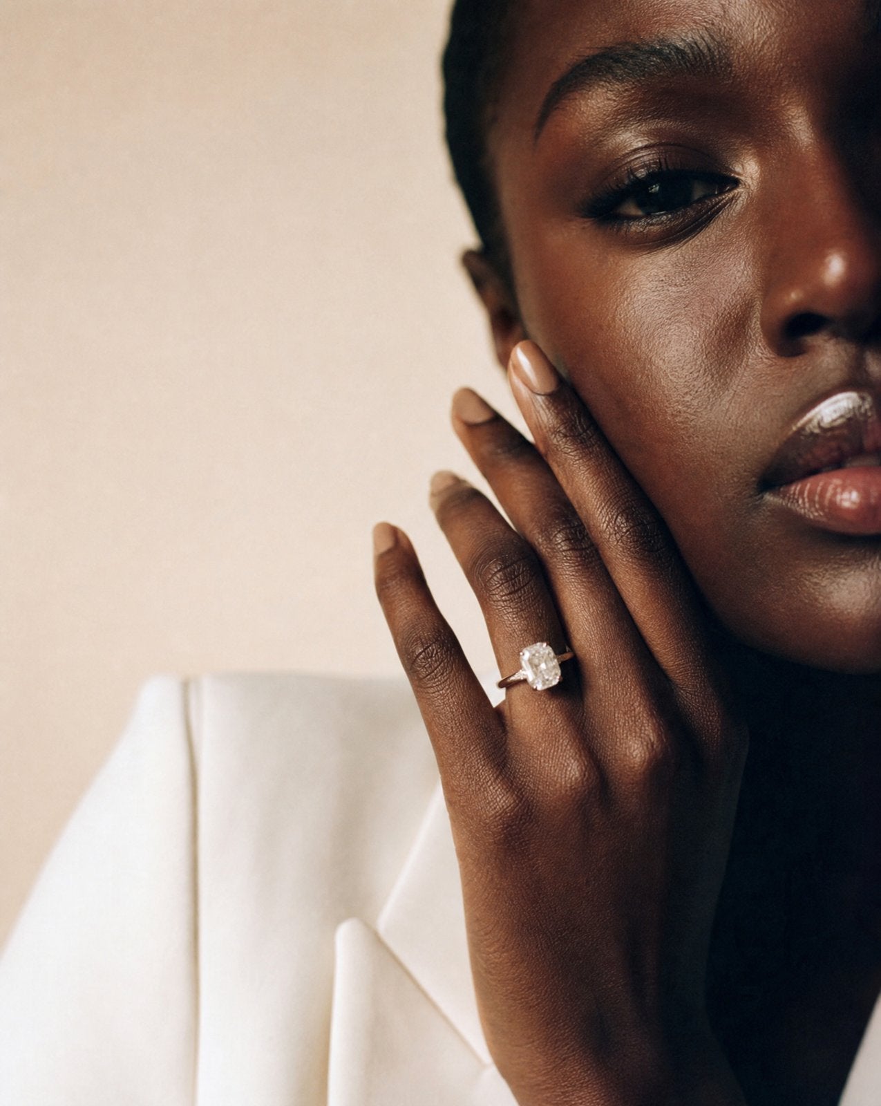 Woman in a white blazer with her hand at her face wearing a lab-grown diamond solitaire ring
